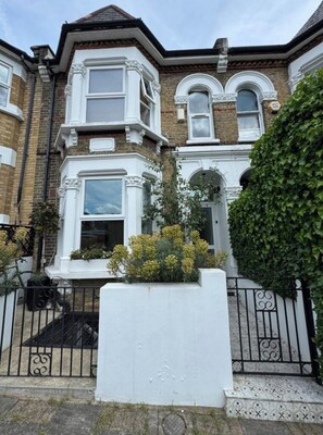 A corner house with a bay window, a white front door, and a small garden area with yellow flowers.