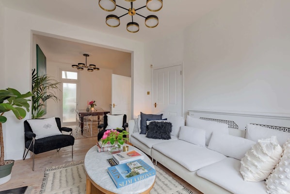 A living room with a white sofa, a black armchair, a round coffee table with books, and a modern chandelier.
