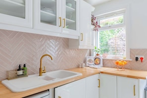 A kitchen with white cabinets, a herringbone tile backsplash, a gold faucet, and a window with a view of greenery.