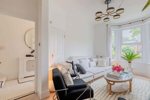 A living room with a sofa, a black armchair, a coffee table, and a ceiling light fixture. - Luxuriously Curated 4BD Home, Stoke Newington (Greater London)