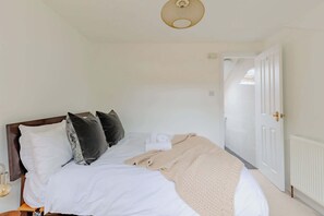A neatly made bed with a beige blanket, a wooden headboard, and several pillows.