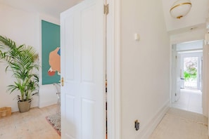A hallway with a white door, a potted plant, and a framed picture on the wall. - Luxuriously Curated 4BD Home, Stoke Newington (Greater London)