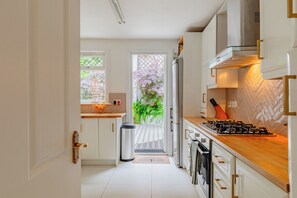 A modern kitchen with white cabinetry, a gas stove, and a view of a garden through the door. - Luxuriously Curated 4BD Home, Stoke Newington (Greater London)