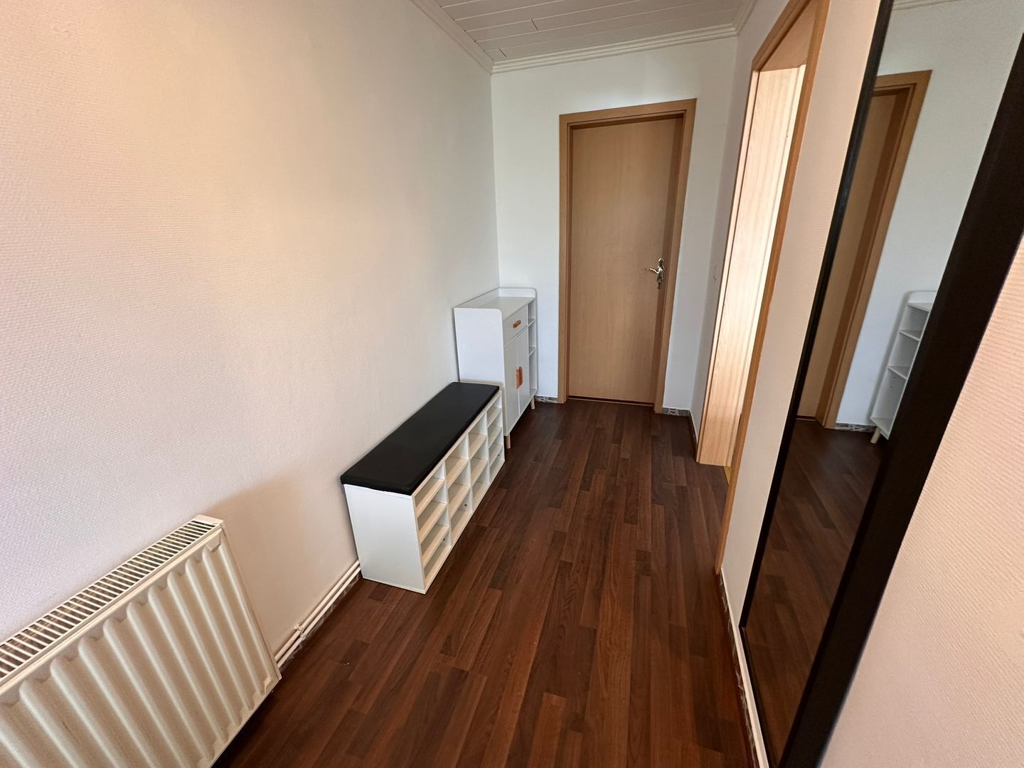 A hallway with a radiator, a white bench, and a door at the end.