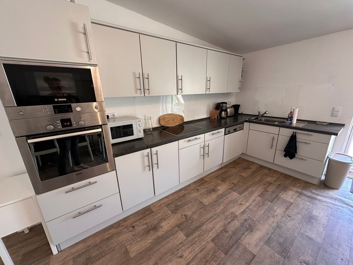 A modern kitchen with white cabinets, stainless steel appliances, and a herringbone wood floor.