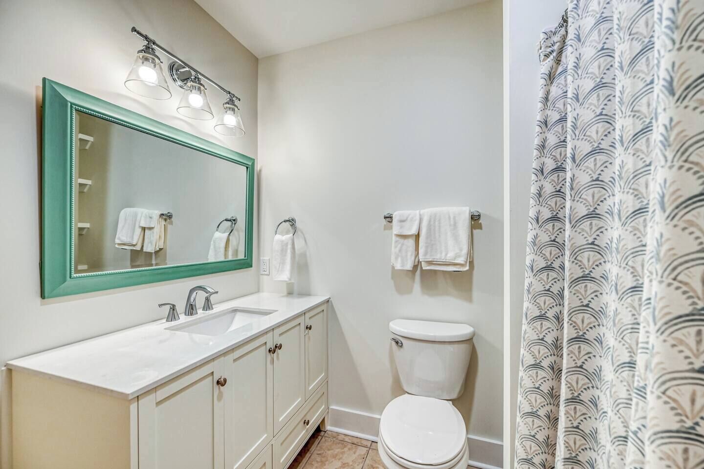 A bathroom with a white sink, green-framed mirror, and a white toilet.