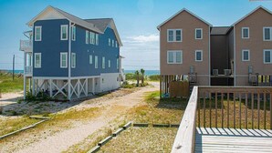A beachfront property with two multi-story houses, one with a balcony and a wooden deck.