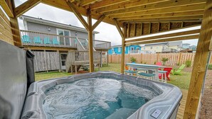 A hot tub in a backyard with a wooden deck, a covered seating area, and a view of neighboring houses.