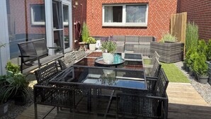 Un patio con mesa de vidrio, mobiliario de mimbre y plantas en macetas.