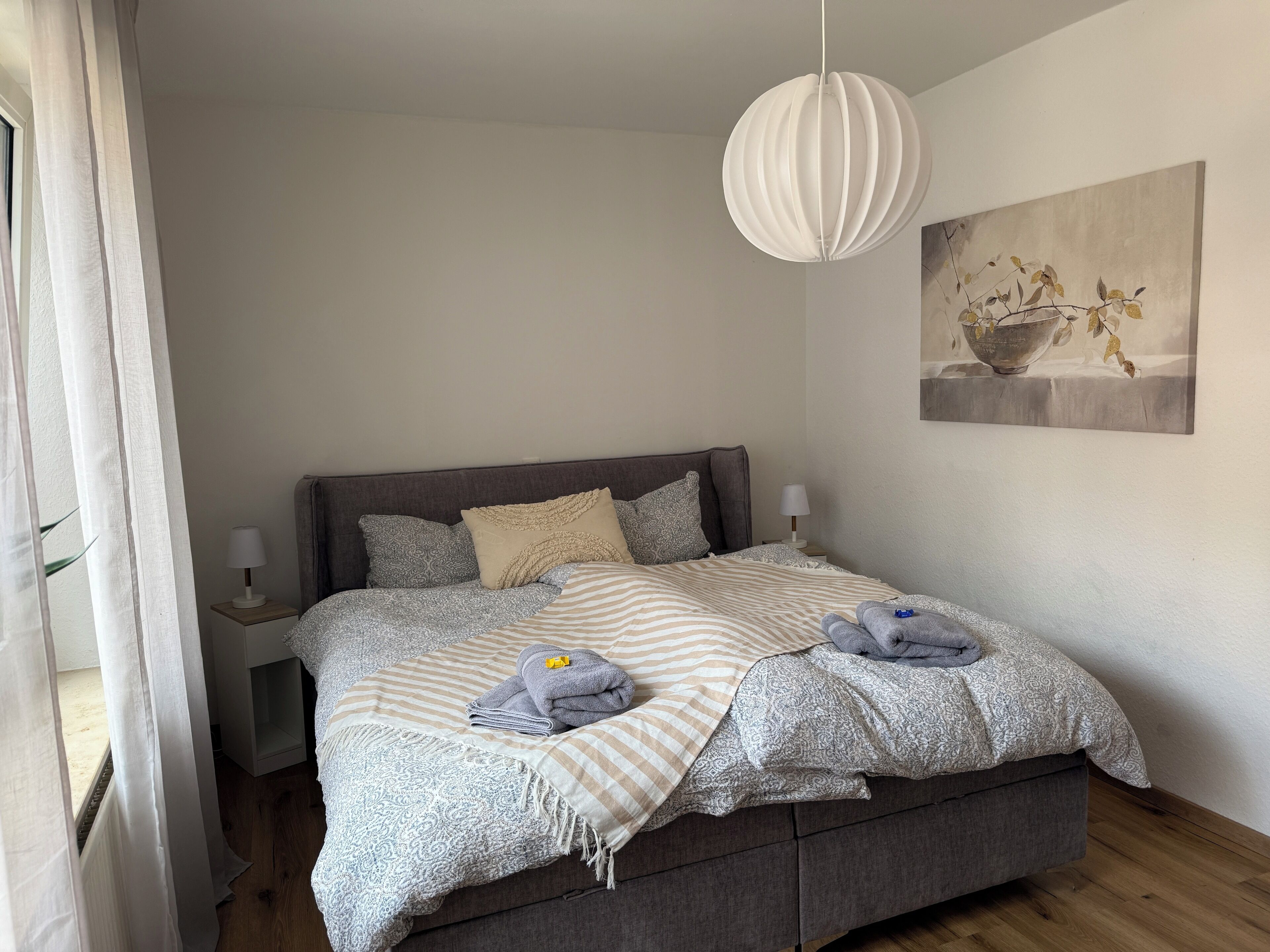 A bedroom with a bed, bedside tables, a hanging light fixture, and a painting on the wall.