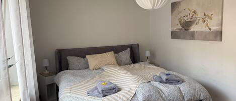 A bedroom with a bed, bedside tables, a hanging light fixture, and a painting on the wall.