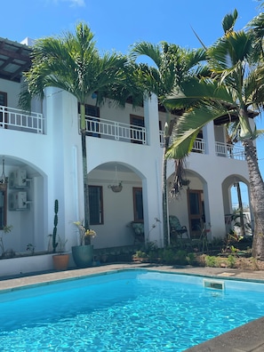 A white building with balconies, a swimming pool, and palm trees.