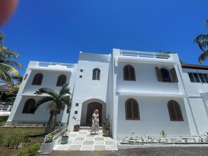 A white building with arched windows and a balcony, surrounded by palm trees.