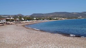A pebble beach with sun loungers and umbrellas, a clear blue sea, and buildings in the background. - Horizon-Amazing location & Seaview! (Latchi)