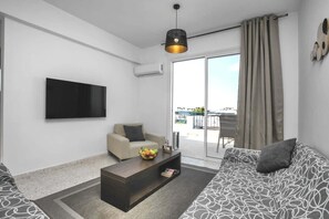 Een moderne woonkamer met een bank, een salontafel met fruit, een televisie en een balkon met uitzicht.