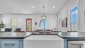 Una cocina moderna con una isla grande, armarios blancos y un lavaplatos de acero inoxidable.