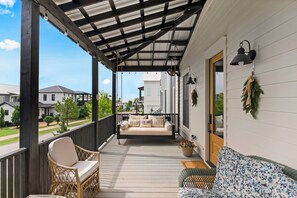 A covered porch with a sofa, wicker chairs, and a potted plant.