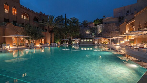 A swimming pool with tiled flooring, surrounded by lounge chairs and umbrellas, with buildings in the background. - AMANAR Ouarzazate Boutique Hôtel & SPA  (Ouarzazate)