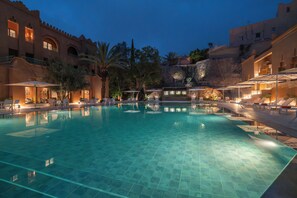 A swimming pool with tiled flooring, surrounded by lounge chairs and umbrellas, with buildings in the background. - AMANAR Ouarzazate Boutique Hôtel & SPA  (Ouarzazate)