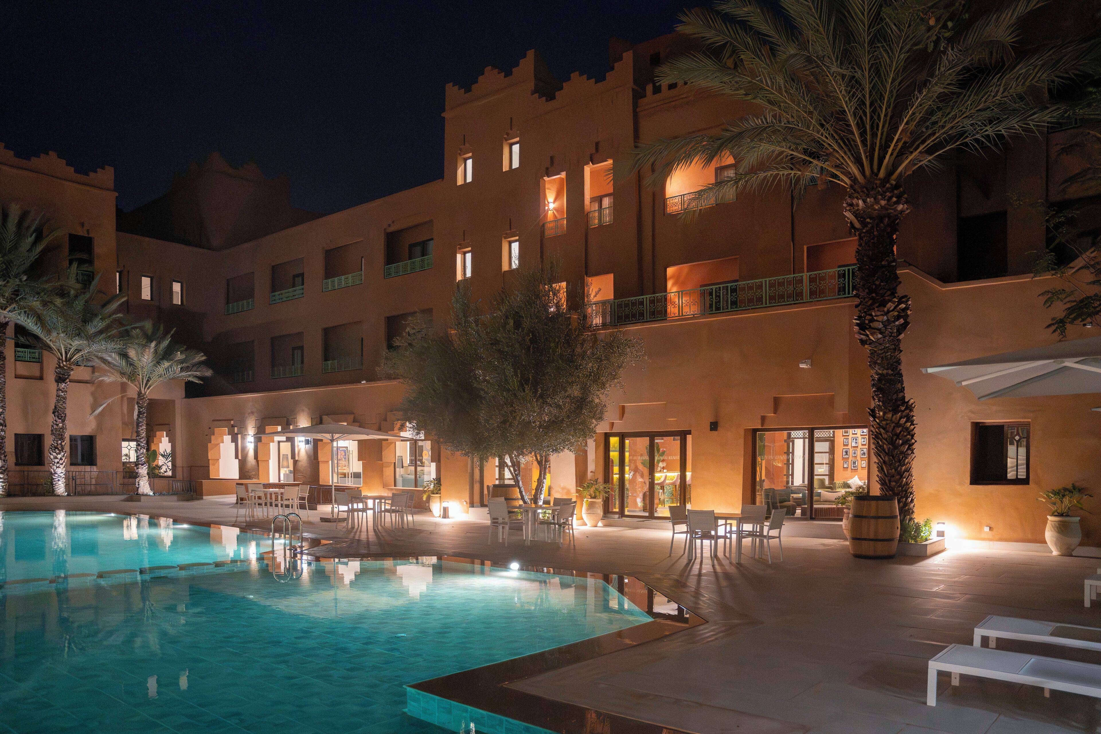 Un patio de hotel con piscina, mobiliario exterior y palmeras.