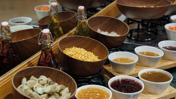 A buffet table with various food items and condiments in bowls and bottles.