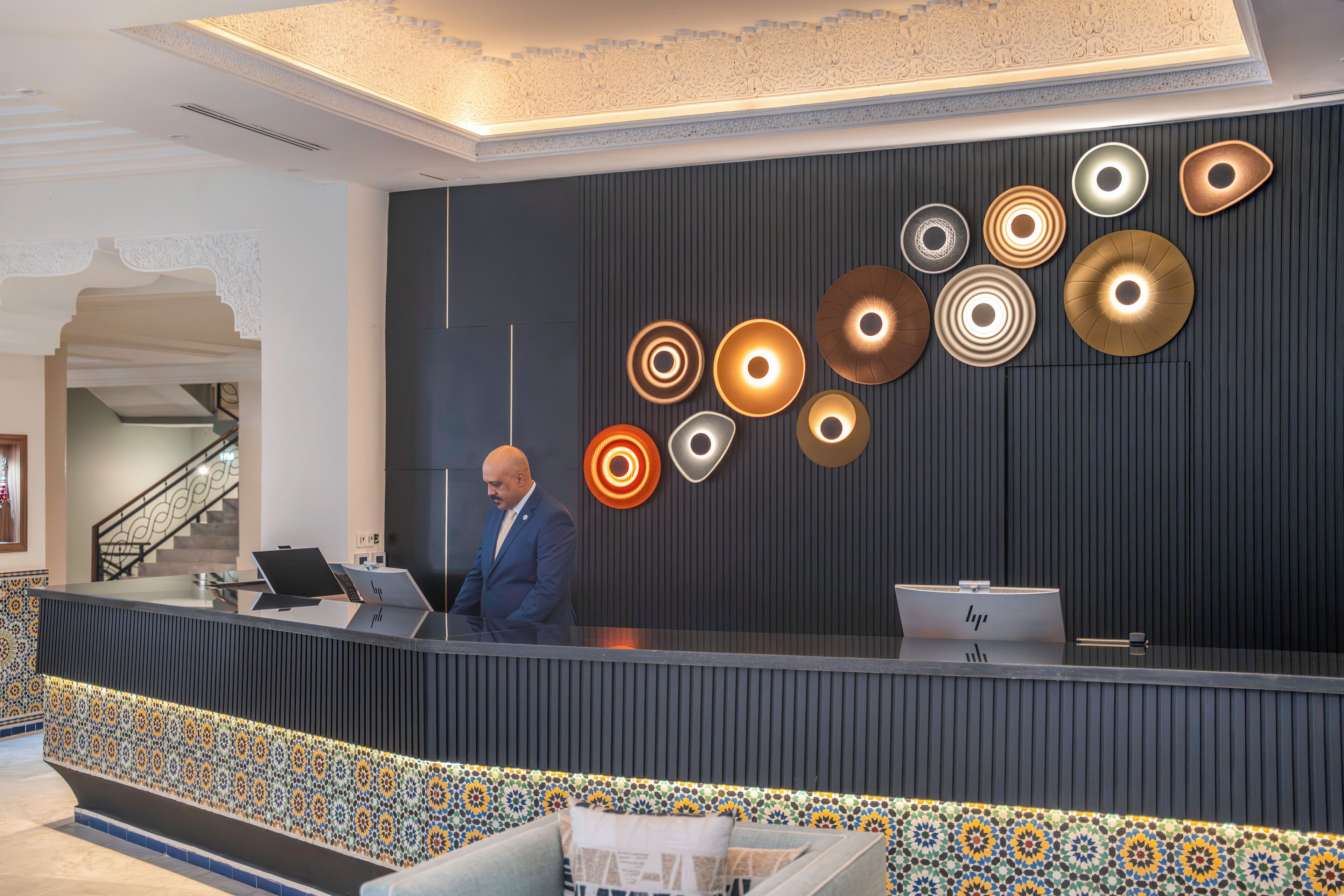 Un'area reception dal design moderno, con una fascia di piastrelle decorate, una scrivania e un lampadario a parete.