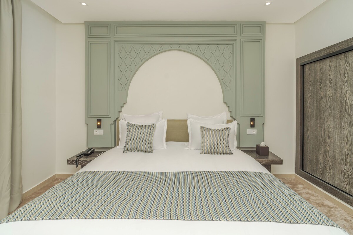 A hotel room with a large bed, two bedside tables, a nightstand, a decorative arch, and a large wooden panel on the wall.