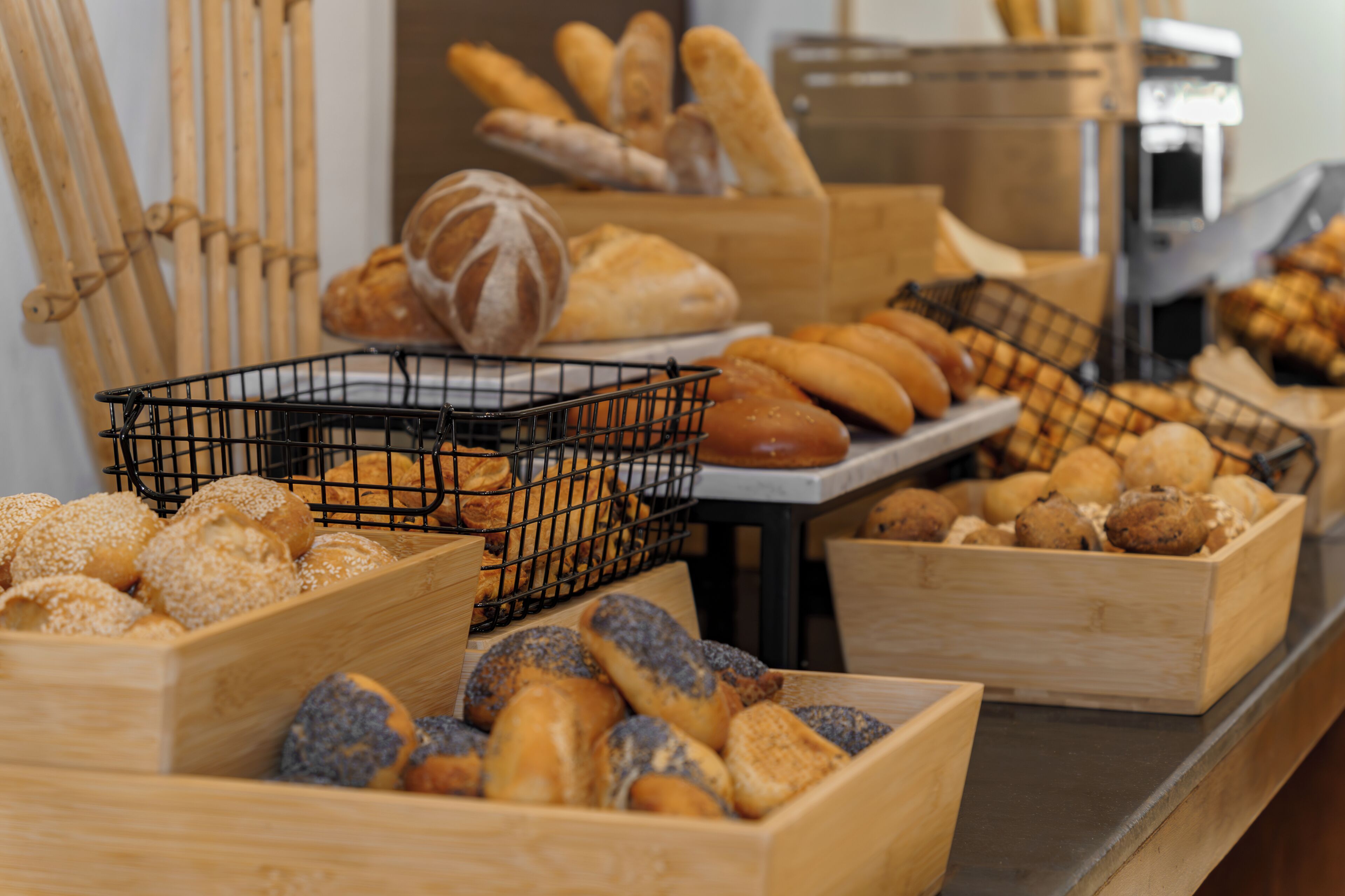 A bakery display with various types of bread and pastries in wooden boxes and wire baskets.