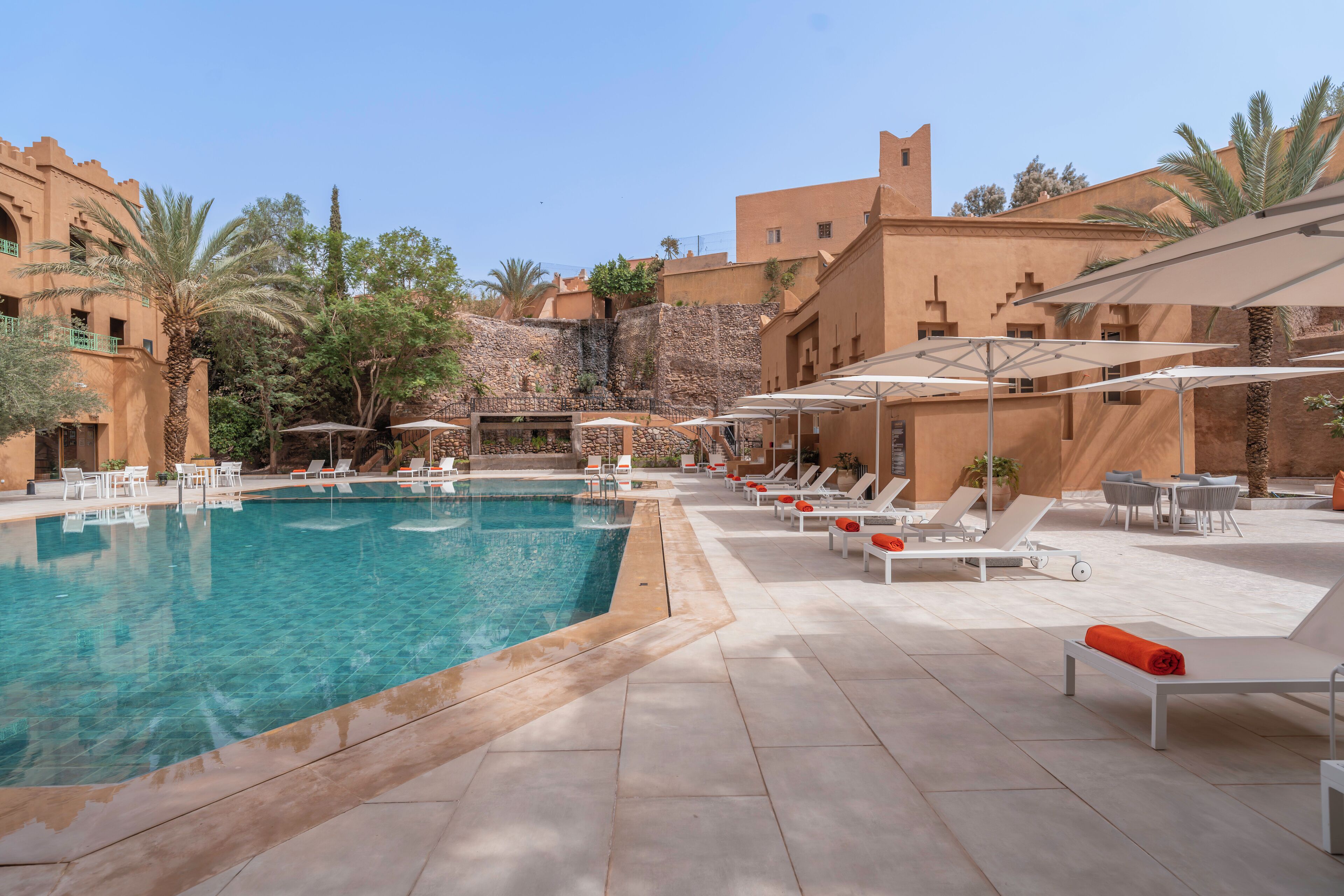 A pool area with clear water, white lounge chairs, and umbrellas.