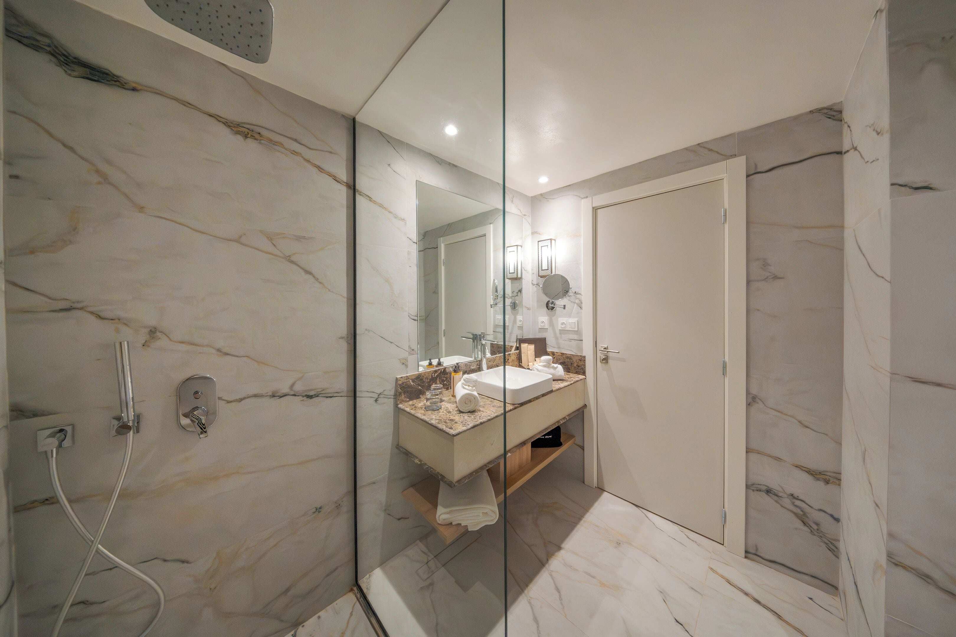A modern bathroom with a marble vanity, a glass shower enclosure, and a door leading to another room.