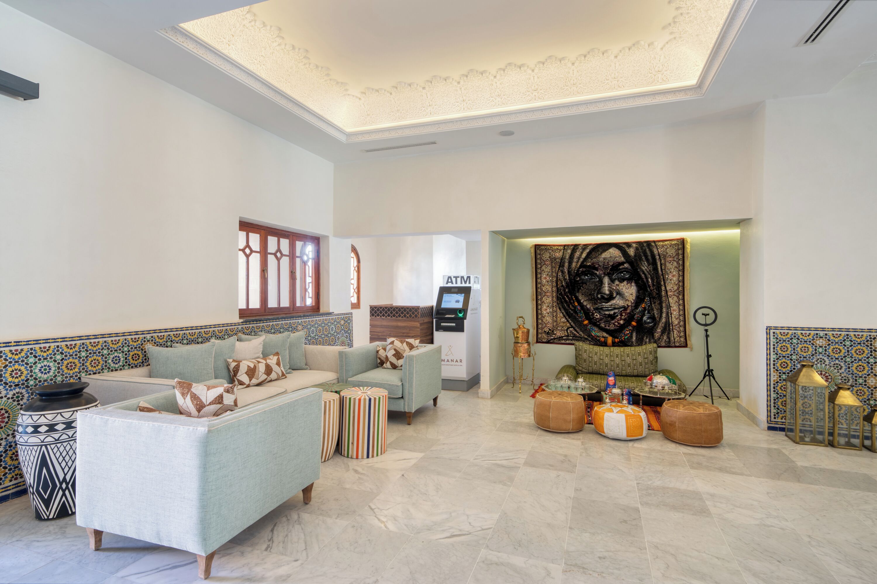 A modern living room with a sofa, ottomans, a wall-mounted ATM, and a large abstract painting.