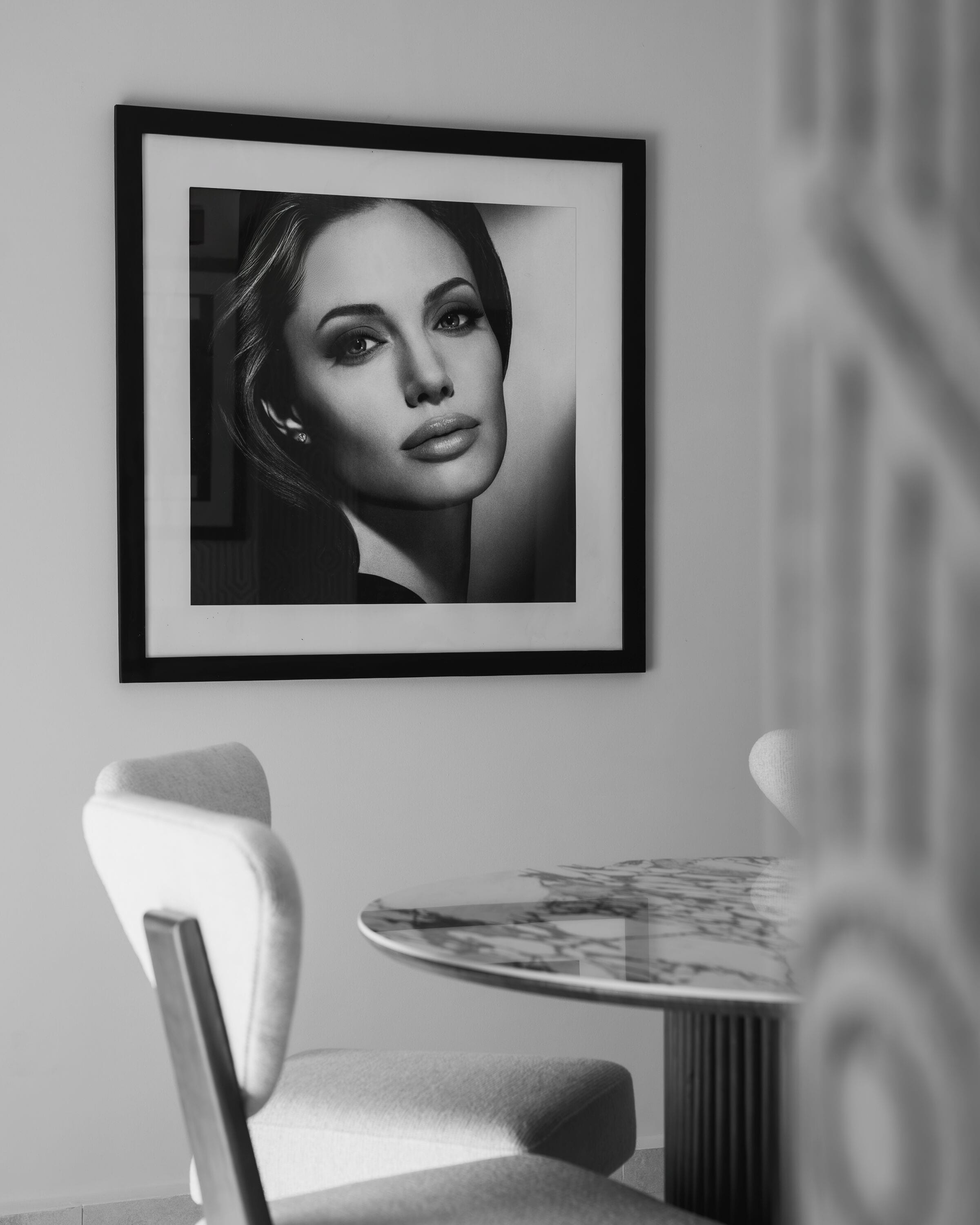 Un portrait encadré accroché au mur, une chaise et une table recouverte d’une nappe à motifs.