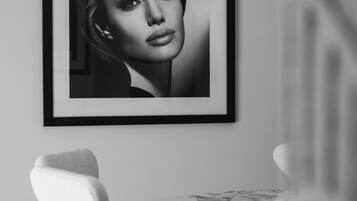 A framed portrait on a wall, a chair, and a table with a patterned tablecloth.