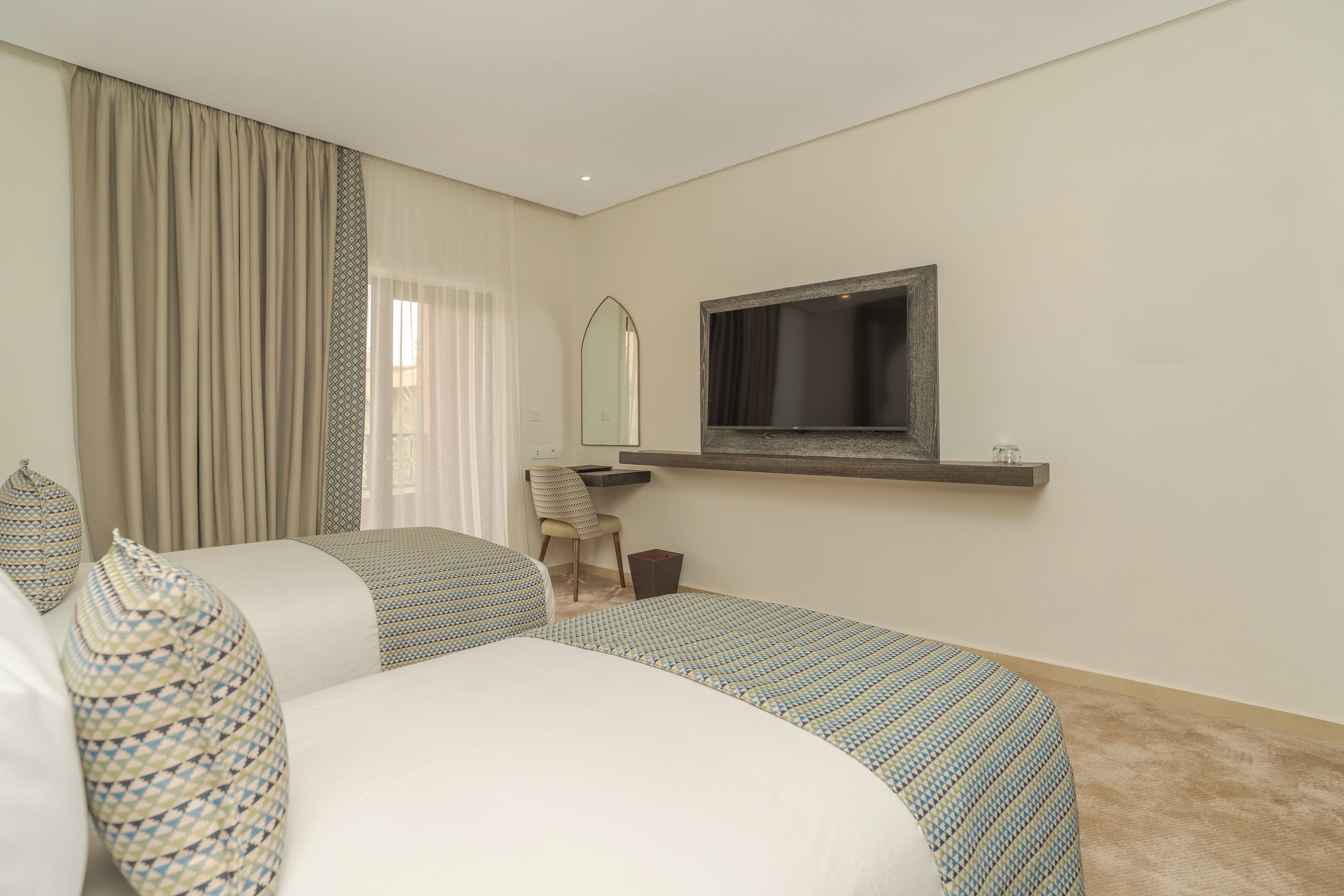 A hotel room with two beds, a desk, a chair, a mirror, and a television.