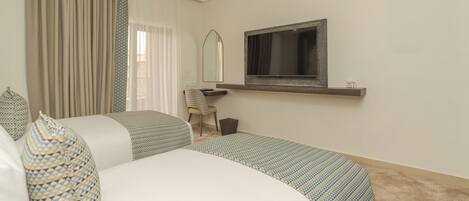 A hotel room with two beds, a desk, a chair, a mirror, and a television.