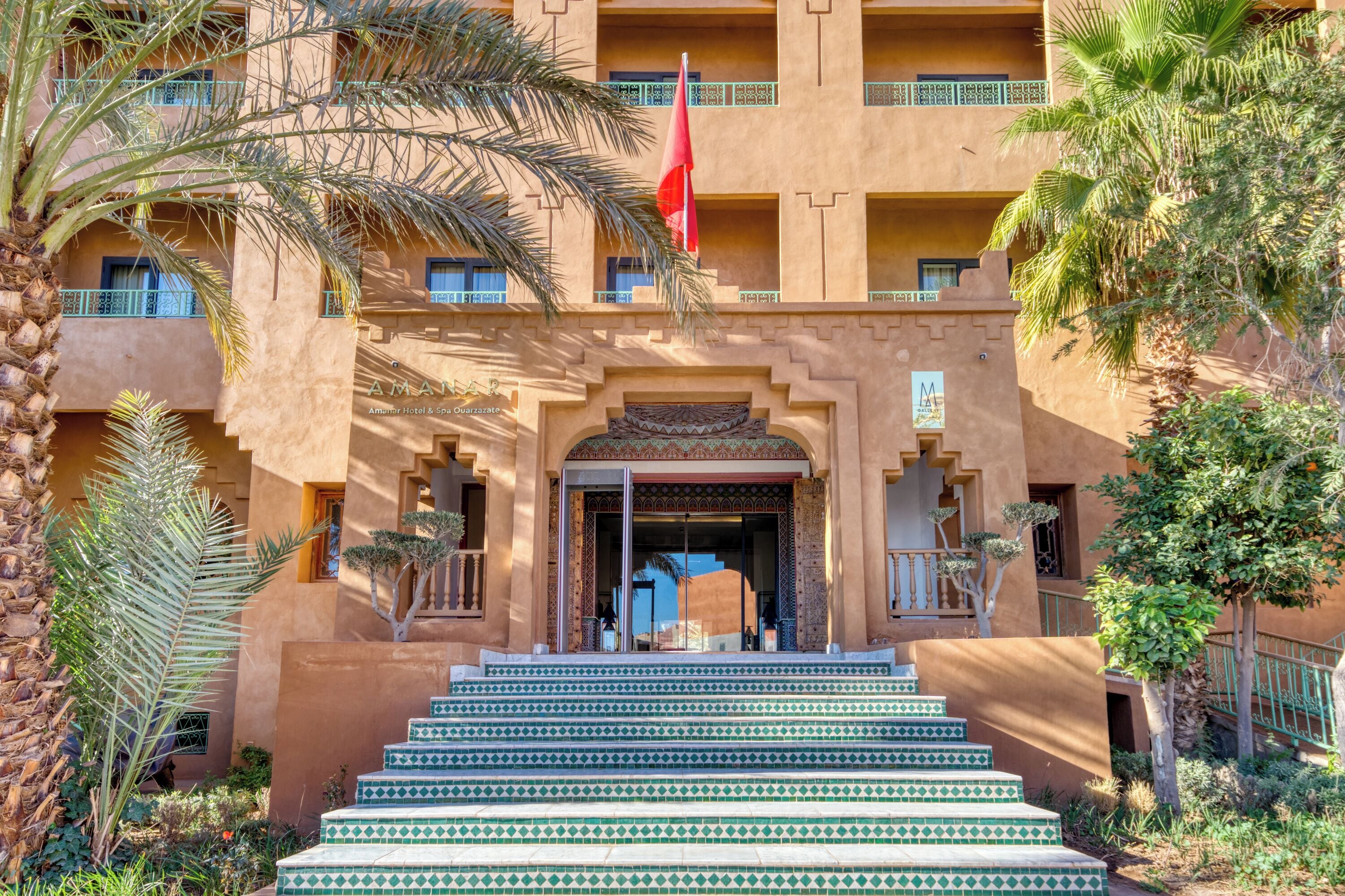 A hotel entrance with a flag, steps, and palm trees.