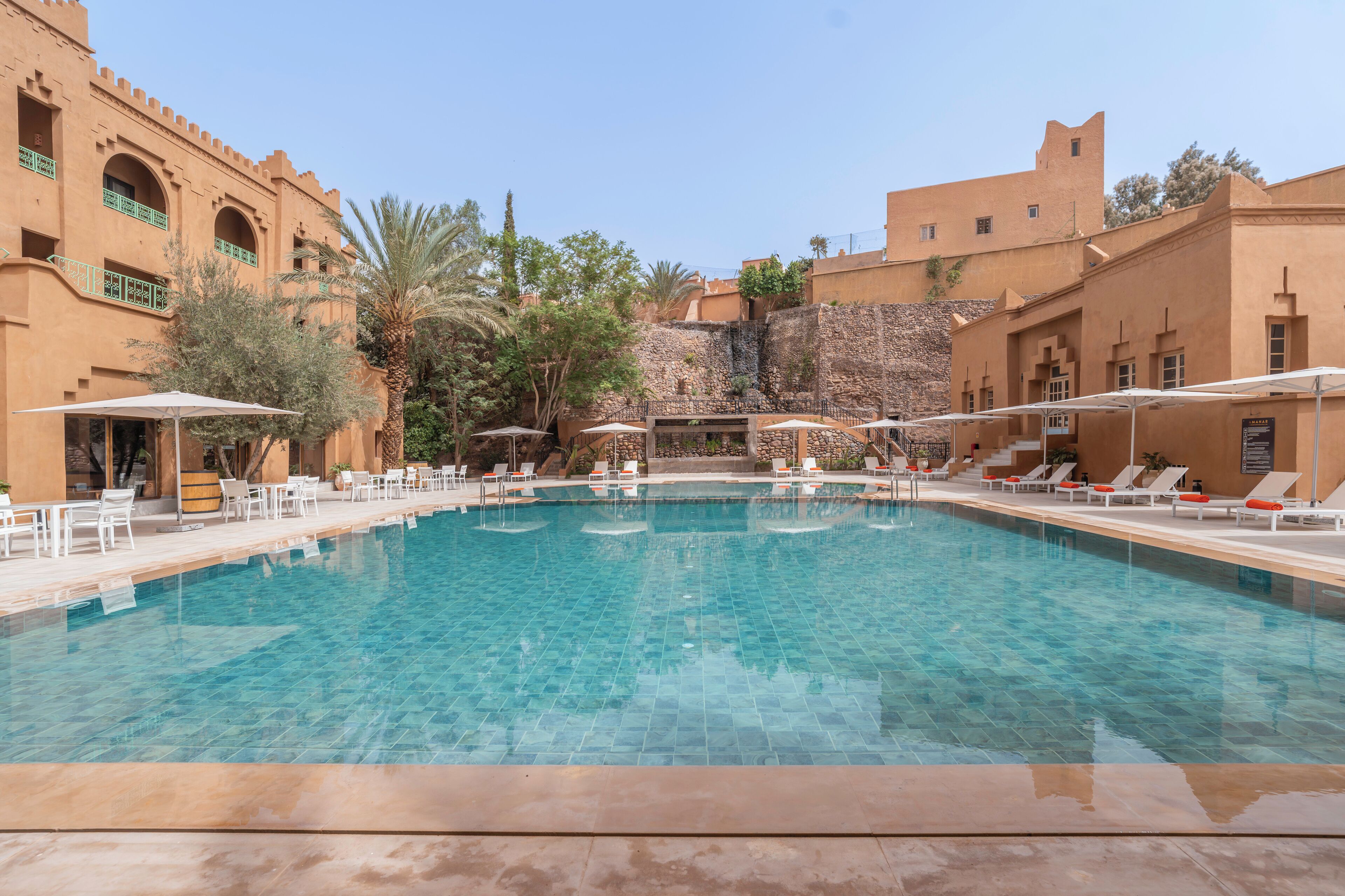A swimming pool with lounge chairs and umbrellas, surrounded by buildings with traditional architecture.