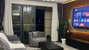 Un salon moderne doté d’un grand téléviseur à écran plat, de canapés gris rembourrés, d’une table basse noire et d’un lustre.