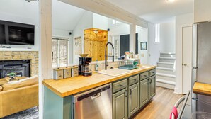 A modern kitchen with a dishwasher, wooden cabinets, and a stone fireplace. - Steps to Jack Frost Ski Resort: Townhome w/ Decks (White Haven)