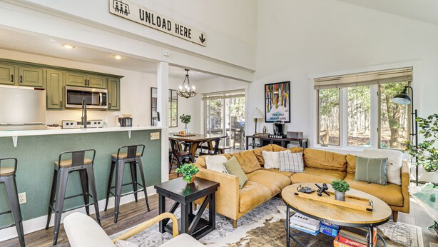 A modern open-plan living and dining area with a kitchen, a sofa, a coffee table, and a bar stool. - Steps to Jack Frost Ski Resort: Townhome w/ Decks (White Haven)