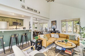 Un espacio moderno y abierto que combina sala de estar, comedor y cocina, con un sofá, una mesa de centro y un taburete de bar.