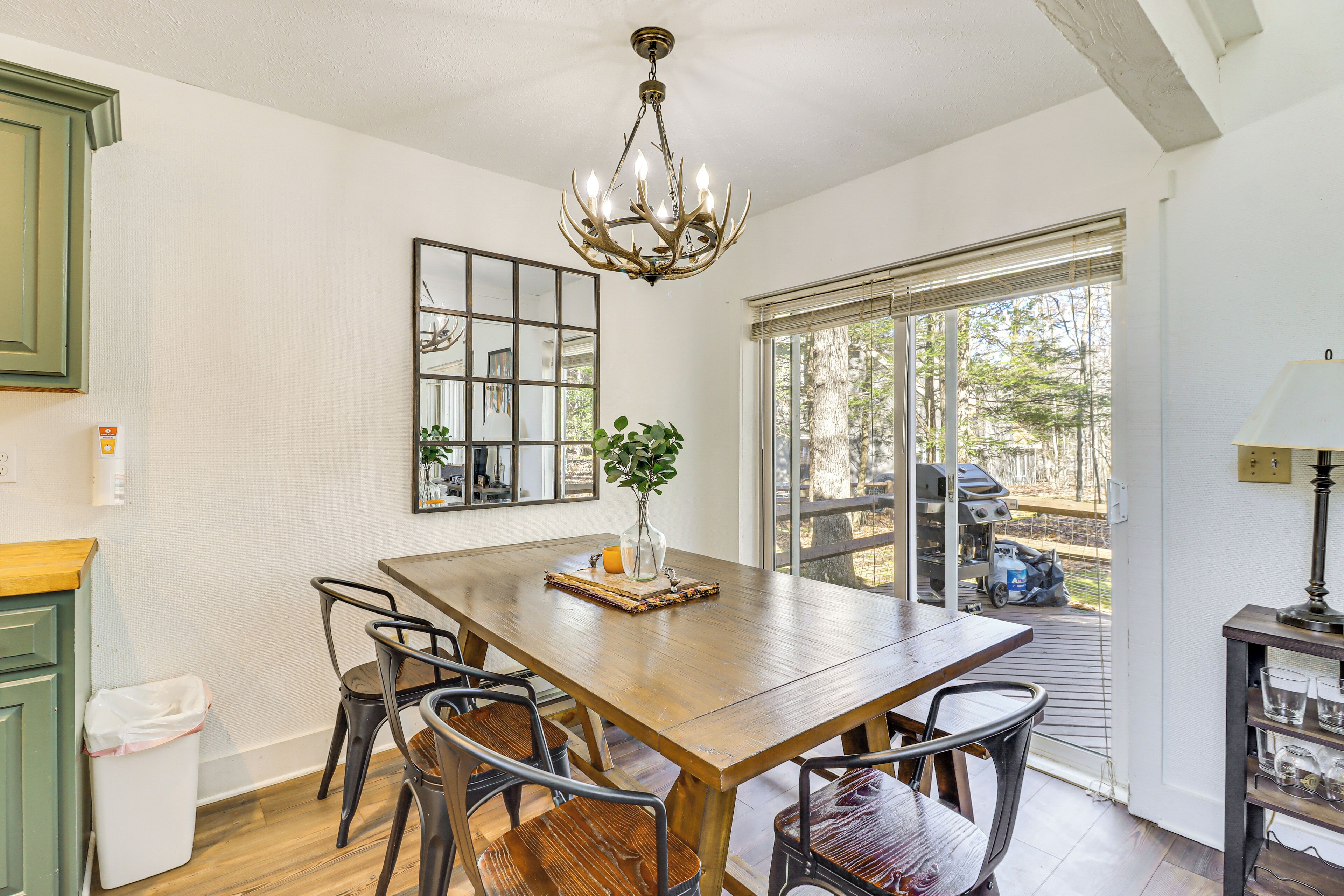 A dining area with a wooden table, metal chairs, a chandelier, and a view of the outdoors.