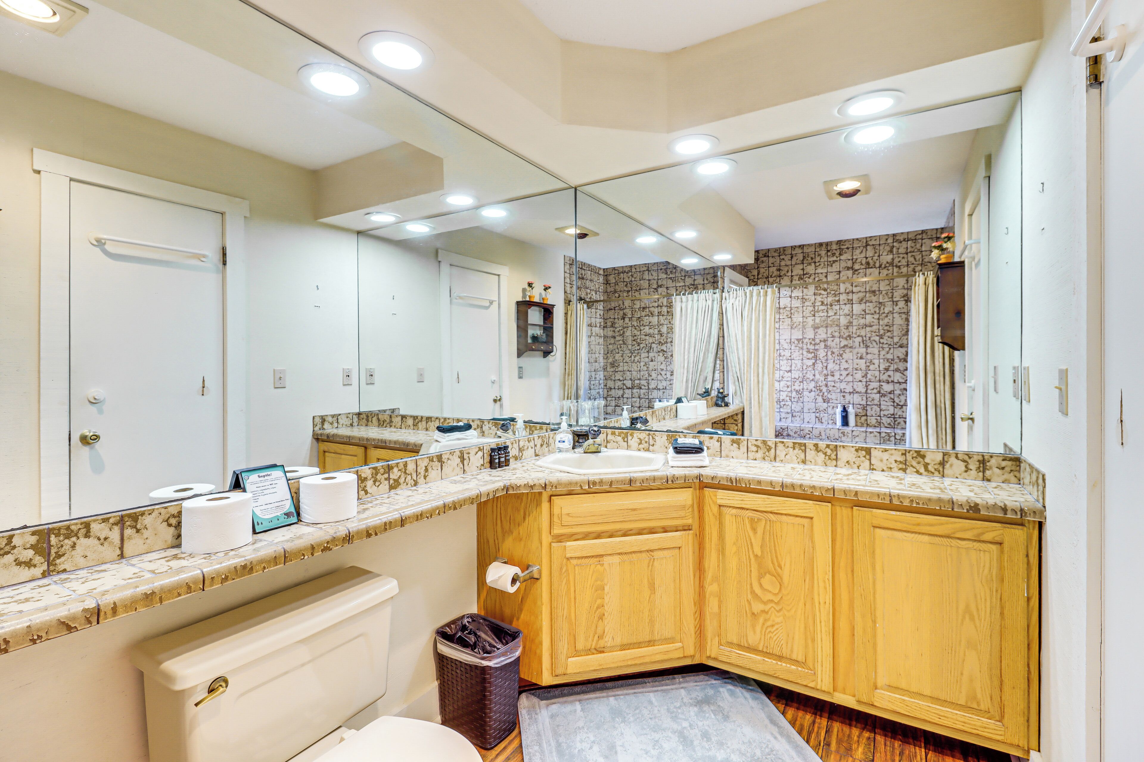 A bathroom with a large mirror, wooden cabinets, a sink, and a toilet.