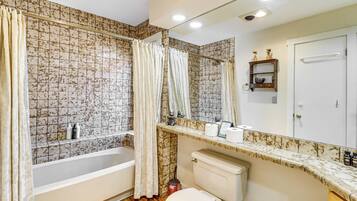 A bathroom with a bathtub, toilet, and a shower curtain. There is a shelf with toiletries and a mirror above the sink.