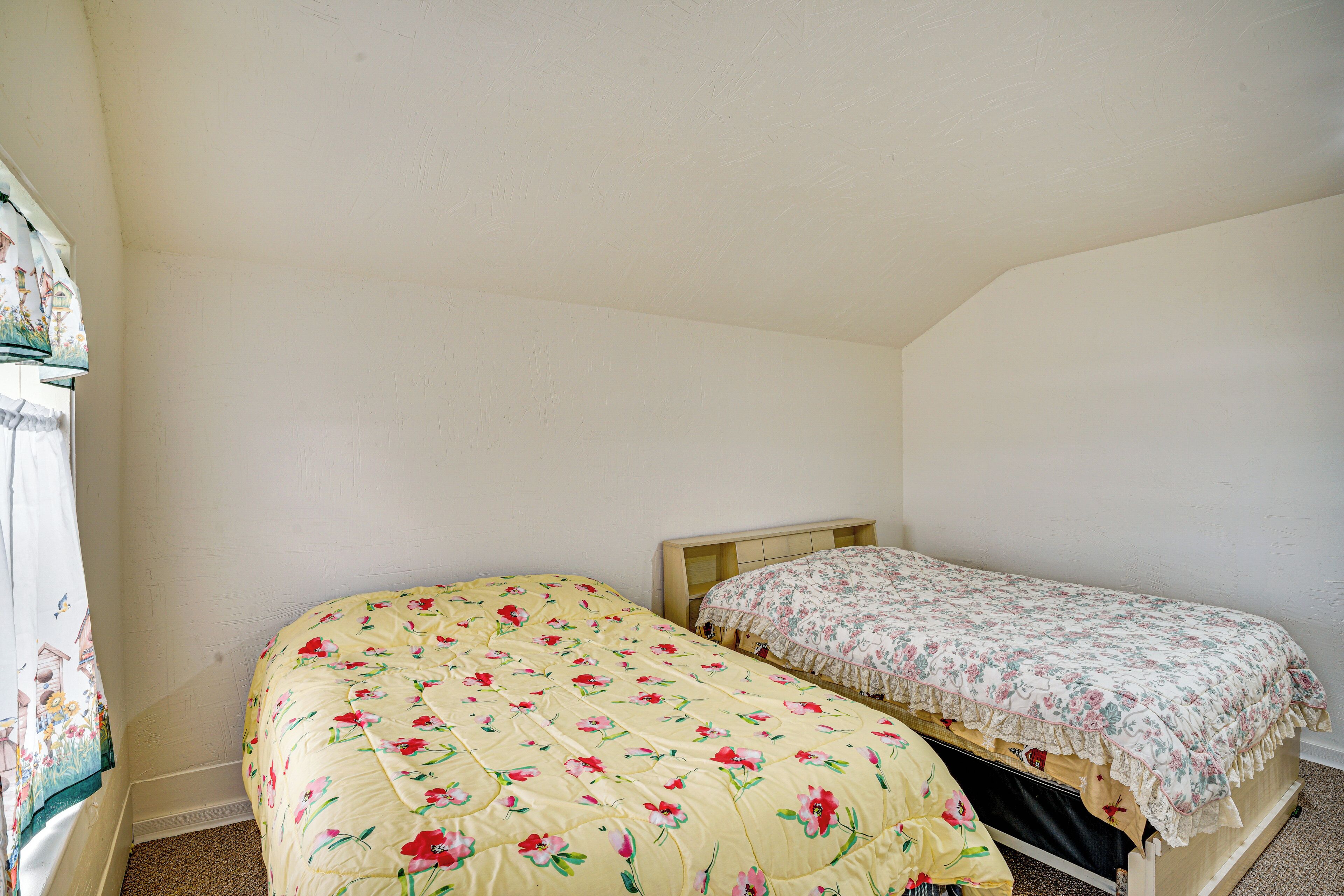 A small bedroom with two single beds, a window with a curtain, and a wooden headboard.