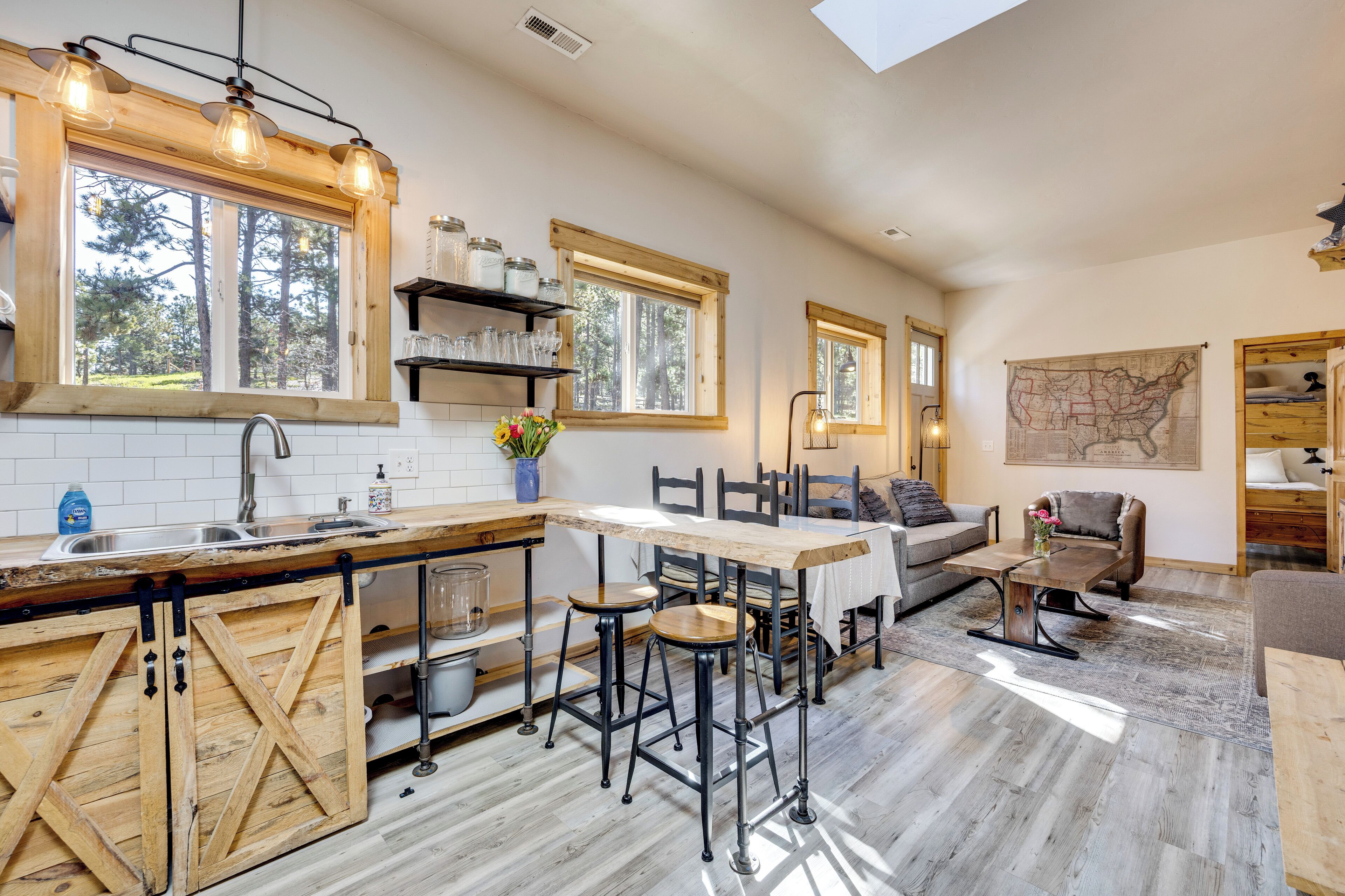 A spacious kitchen with wooden cabinets, a large island, and a dining area with a table and chairs. There are multiple windows providing natural light and a view of the outdoors.