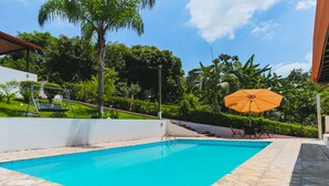 Une piscine à l’eau d’un bleu cristallin, entourée d’un mur blanc, et un espace patio avec une chaise et un parasol.