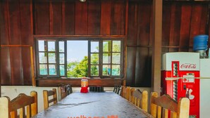 Une pièce rustique en bois, avec une longue table, des chaises, une fenêtre et un vieux réfrigérateur Coca-Cola.