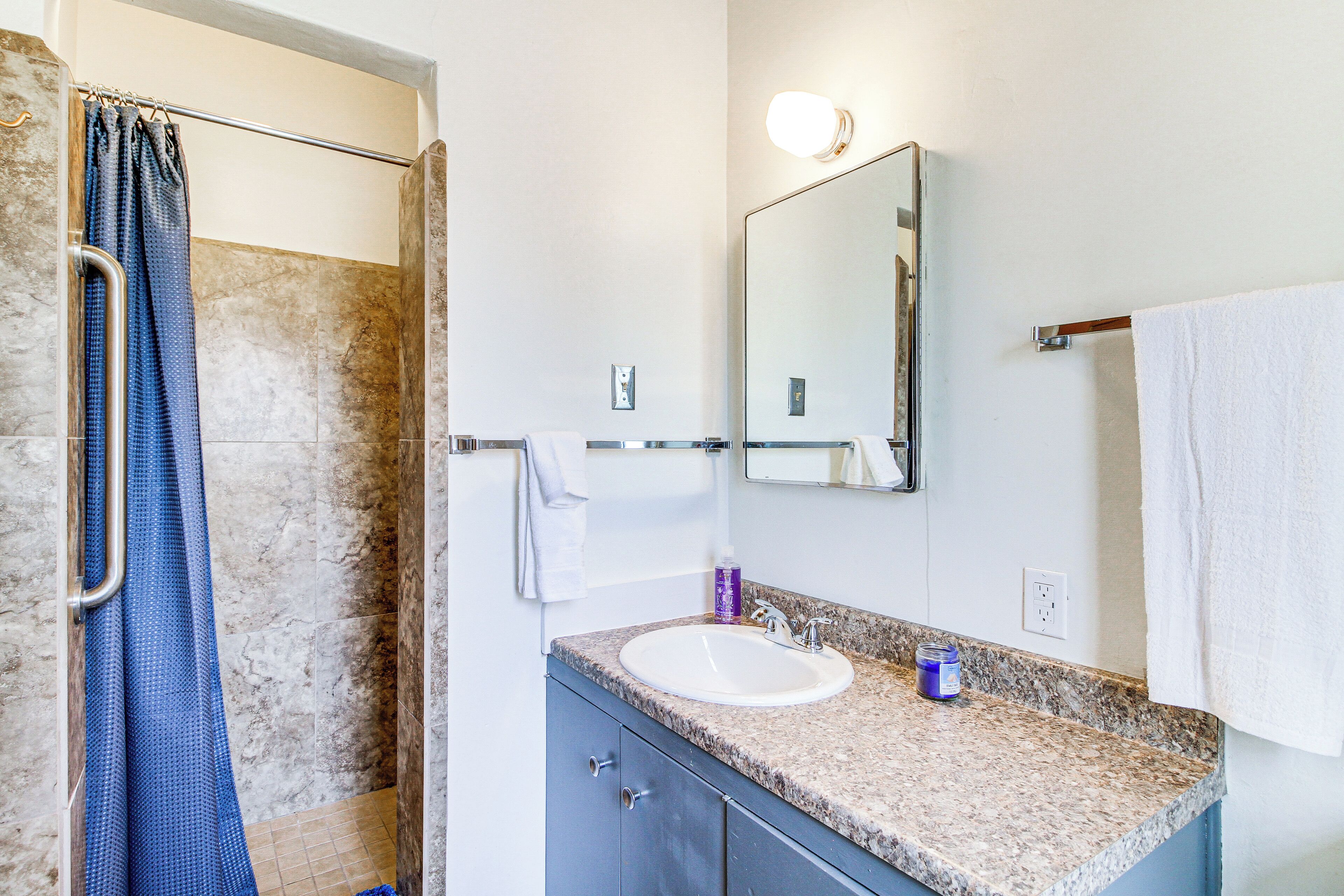 A bathroom with a shower, a sink, a mirror, and a towel rack.