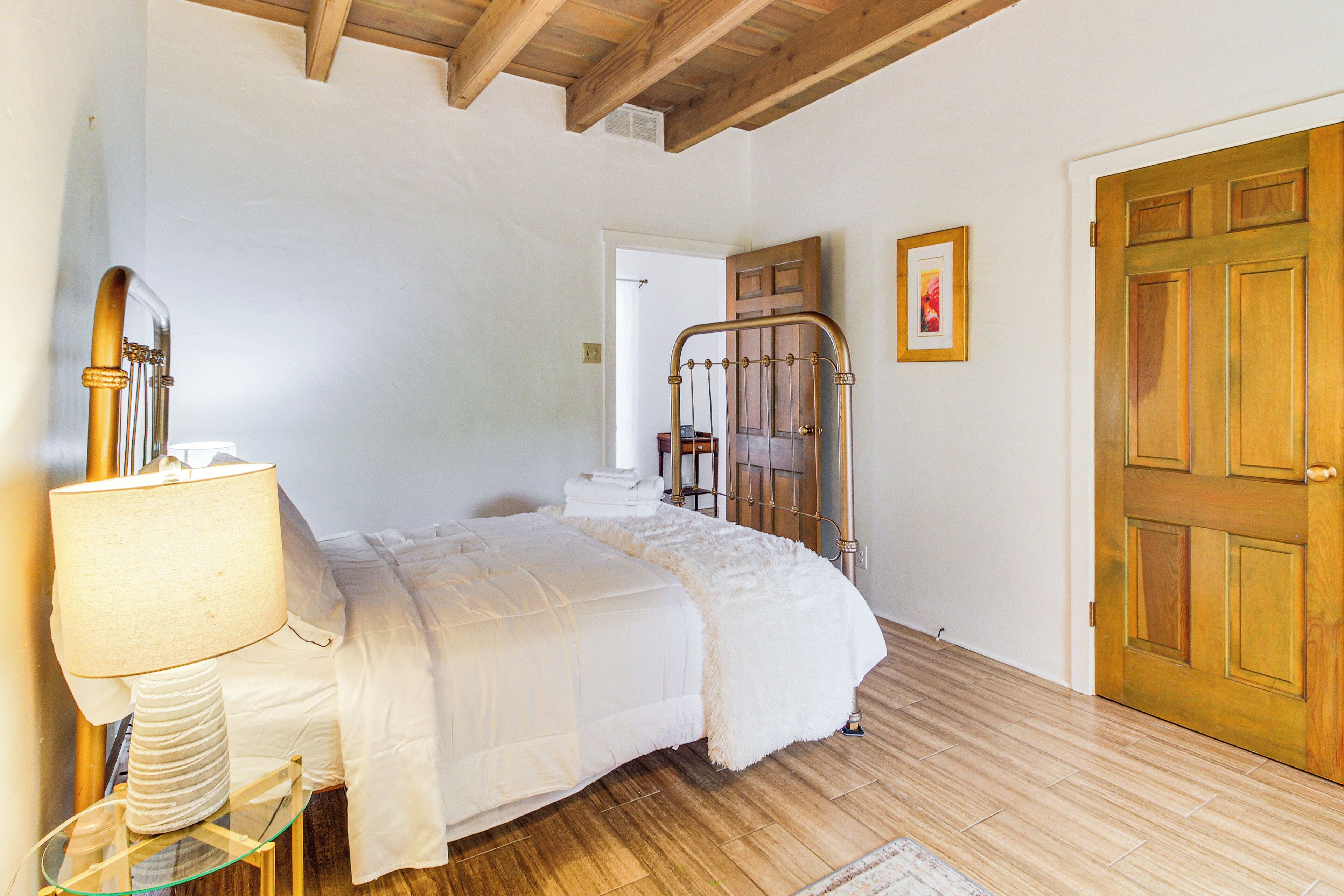 A bedroom with a bed, a bedside table with a lamp, a wooden door, and a framed picture on the wall.